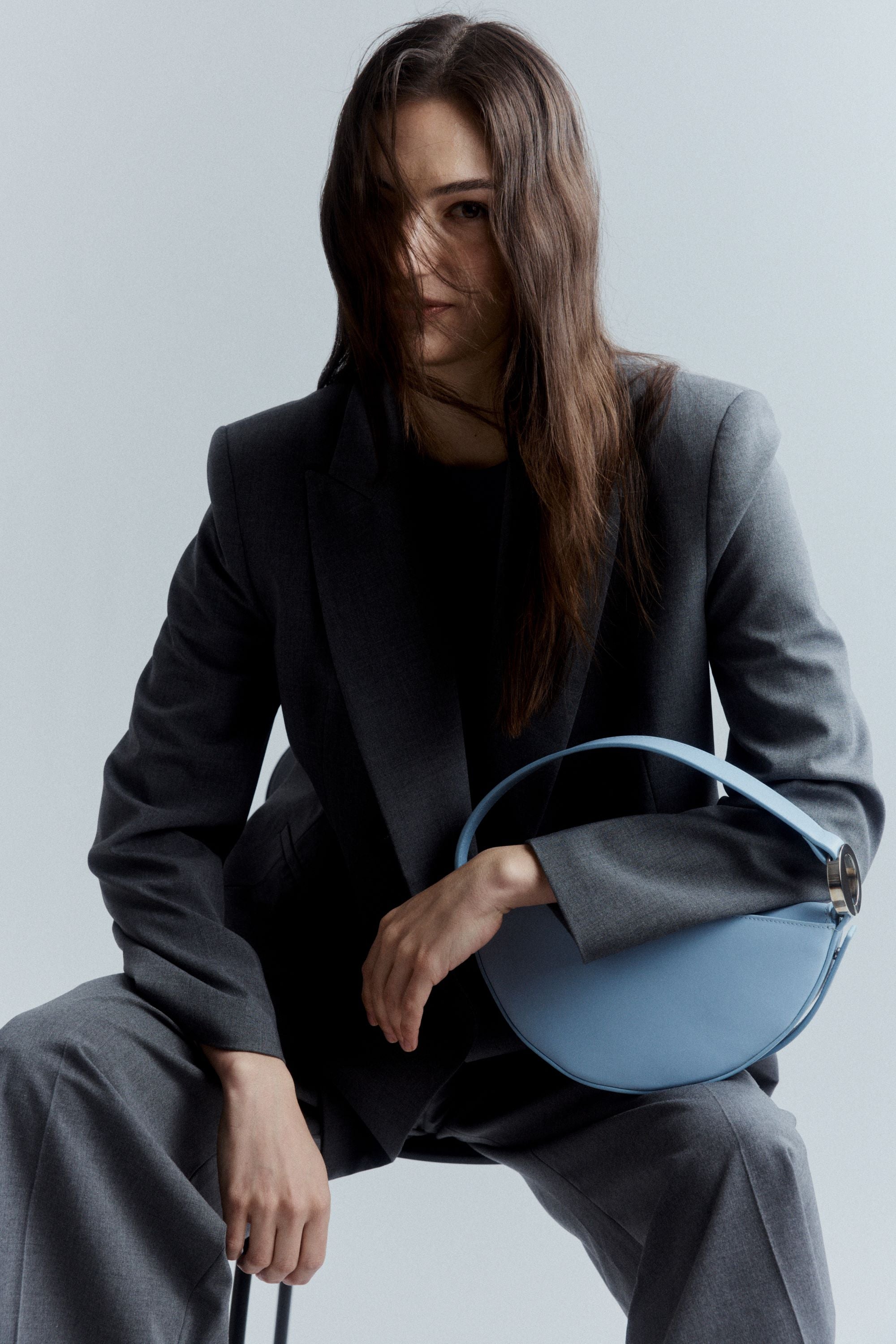 Woman holding a blue handbag against a plain background